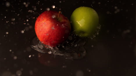 Green-and-red-apples-falling-on-wet-black-surface