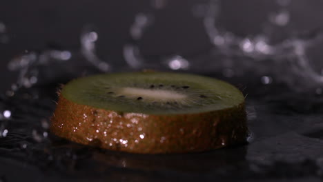 Kiwi-slice-falling-on-wet-black-background