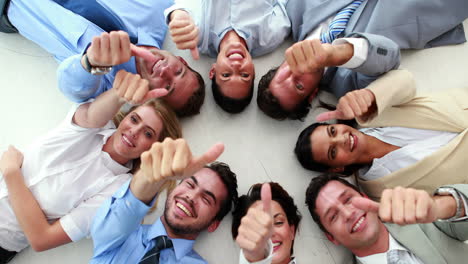 Business-people-lying-in-a-circle-showing-thumbs-up