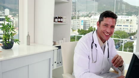 Handsome-doctor-working-at-his-desk-smiling-at-camera