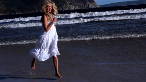 Beautiful-blonde-running-in-white-dress-on-sunny-day-at-the-beach