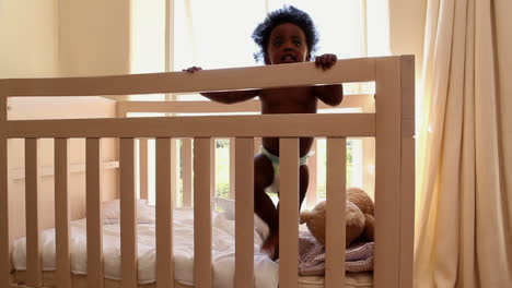 Cute-baby-girl-standing-in-her-crib-looking-at-camera