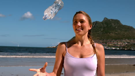 Fit-blonde-smiling-and-throwing-her-bottle-on-the-beach