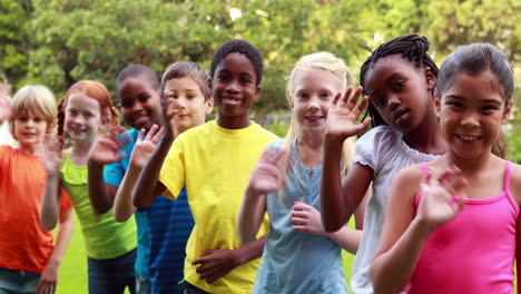 Row-of-cute-pupils-waving-and-smiling-at-camera