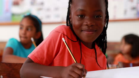 Kleines-Mädchen-Schreibt-Und-Lächelt-Während-Des-Unterrichts-In-Die-Kamera
