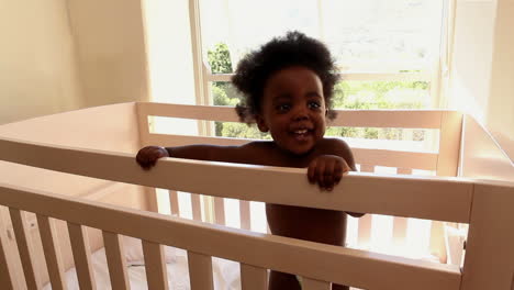 Cute-baby-girl-standing-in-her-crib-looking-at-camera