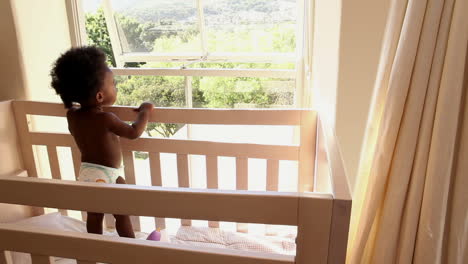 Cute-baby-girl-standing-in-her-crib-looking-out-window