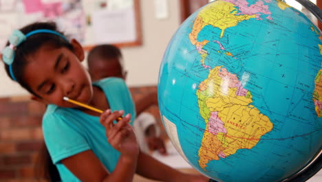 Little-girl-looking-at-globe-and-writing-in-classroom