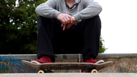 Young-skateboarder-sitting-at-the-outdoor-skatepark
