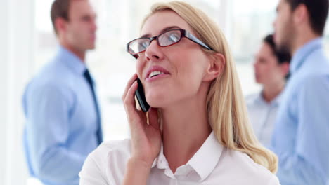 Businesswoman-talking-on-phone-with-colleagues-behind-her