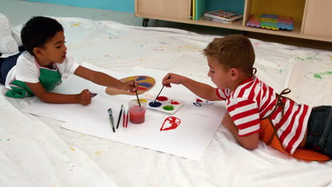 Cute-little-boys-painting-lying-on-paper-in-classroom