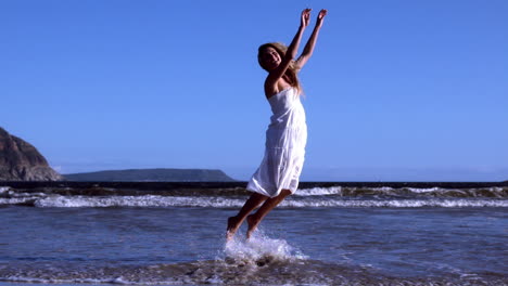 Schöne-Blondine-Springt-Im-Weißen-Kleid-An-Einem-Sonnigen-Tag-Am-Strand