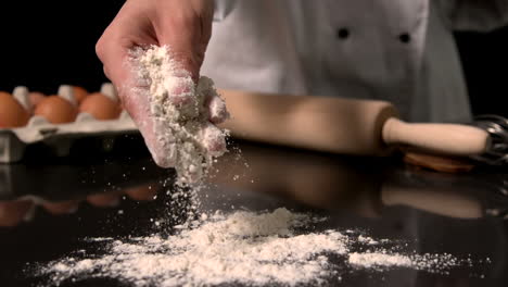 Chef-sprinkling-flour-on-black-surface