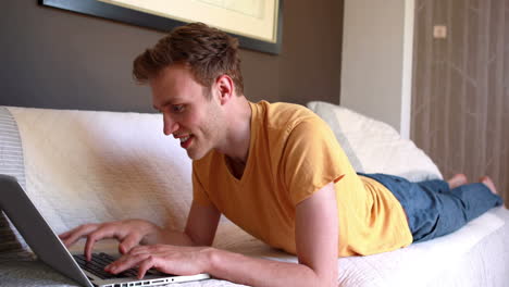 Young-man-lying-on-bed-using-laptop