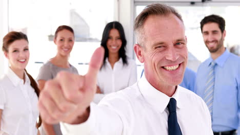 Business-team-smiling-at-the-camera-with-boss-showing-thumbs-up