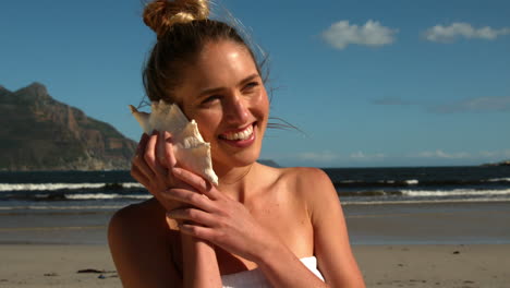 Smiling-blonde-listening-to-conch-on-the-beach