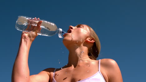 Fit-blonde-drinking-from-water-bottle-on-sunny-day