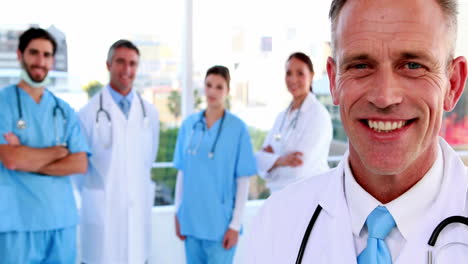 Doctor-smiling-at-camera-with-team-behind-him-