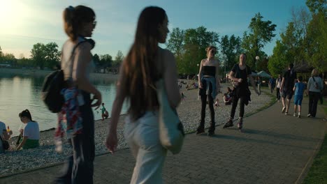 People-enjoying-a-lakeside-beach,-walking,-and-rollerblading-on-a-path-at-sunset-in-Jarun-Lake,-Zagreb