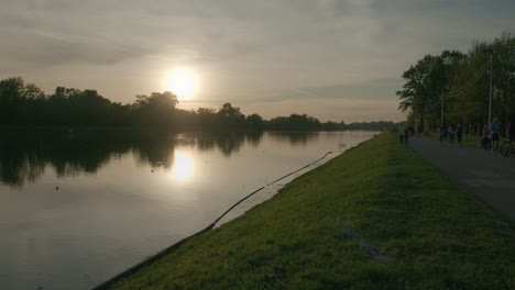 Sonnenuntergang-Spiegelt-Sich-Auf-Einem-Ruhigen-See-Mit-Menschen,-Die-Entlang-Des-Uferwegs-Am-Jarun-See,-Zagreb,-Kroatien-Spazieren