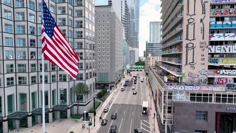 Amerikanische-Flagge-Weht-Mit-Straßenbahn-Im-Vordergrund-In-Miami,-Florida