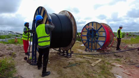 Afrikanische-Techniker-Und-Ingenieure-Wickeln-Stromkabel-Ab-Und-Verlegen-Sie-Auf-Einem-Solarpark-Für-Erneuerbare-Energien-–-Statische-Weitwinkelaufnahme