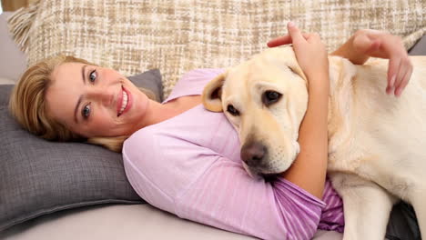 Glückliche-Blondine-Streichelt-Labrador-Auf-Der-Couch