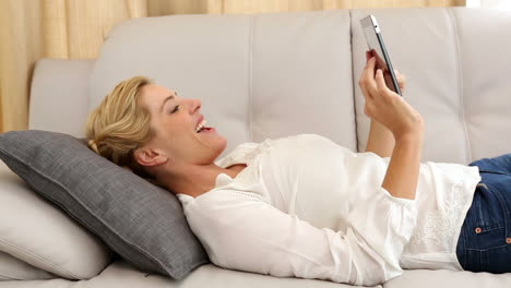 Happy-blonde-using-tablet-pc-on-couch