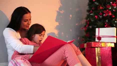 Mother-reading-her-daughter-a-story-by-the-christmas-tree