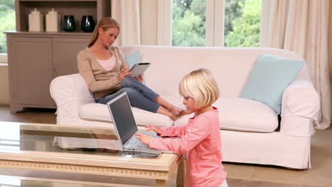 Cute-little-girl-using-laptop-while-mother-uses-tablet