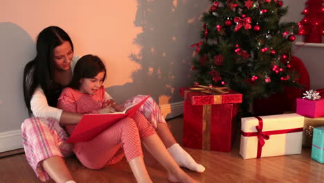 Mother-reading-her-daughter-a-story-by-the-christmas-tree