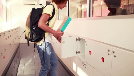 Handsome-student-putting-notebooks-in-his-locker