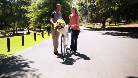 Glückliches-Paar-Zu-Fuß-Mit-Fahrrad-Und-Blumenstrauß