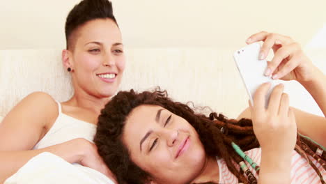Lächelndes-Lesbisches-Paar,-Das-Zusammen-Im-Bett-Smartphone-Benutzt