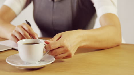 Serious-businesswoman-writing-notes-while-drinking-coffee