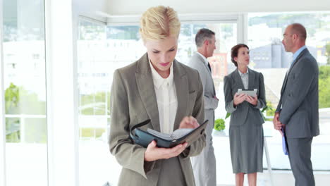 Businesswoman-looking-at-notebook-with-her-colleagues-behind