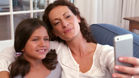 Happy-mother-and-daughter-sitting-on-the-couch-and-taking-selfie