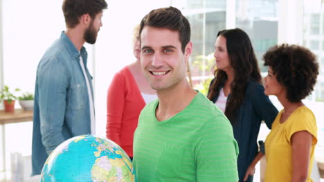 Casual-businessman-holding-terrestrial-globe-with-his-colleagues-behind
