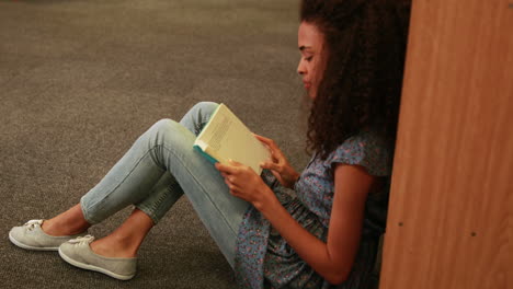 Focused-student-reading-a-book-lying--on-the-floor-