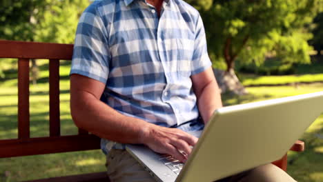 Man-sitting-on-park-bench-and-using-laptop