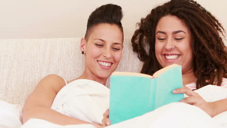 Smiling-lesbian-couple-reading-book-in-the-bed