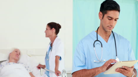 Doctor-Mirando-Usando-Una-Tableta-Mientras-Sus-Colegas-Hablan-Con-El-Paciente-