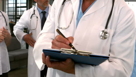 Mid-section-view-of-doctor-writing-on-clipboard