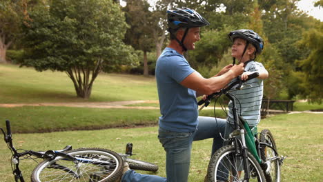 Father-attaching-his-son-cycling-helmet-in-the-park