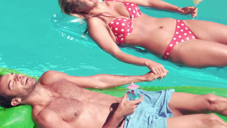 Attractive-couple-relaxing-on-lilos-in-pool