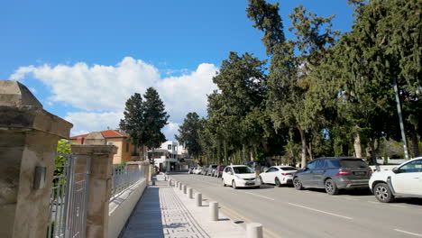 Una-Vista-De-La-Calle-En-Pafos-Con-Autos-Estacionados,-árboles-Altos-Y-Edificios-Residenciales-Bajo-Un-Cielo-Azul-Claro.