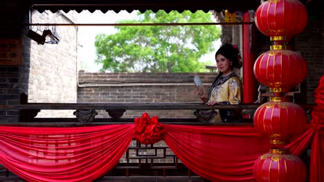 Qing-Dynasty-girl-in-traditional-clothing-smiles-on-a-decorated-Chinese-balcony-in-Pingyao,-China