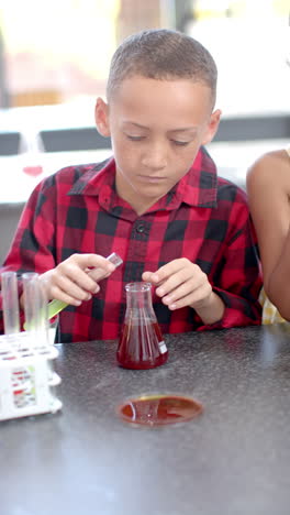 Vertical-Video-of-in-school,-boy-wearing-a-red-checkered-shirt-is-conducting-a-science-experiment