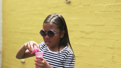 In-a-schoolyard,-a-young-biracial-girl-blowing-bubbles,-yellow-background