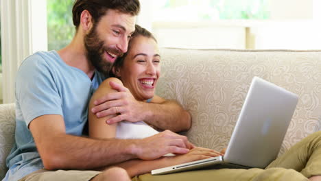 Cute-couple-sitting-on-a-sofa-with-a-laptop-and-embracing-each-other